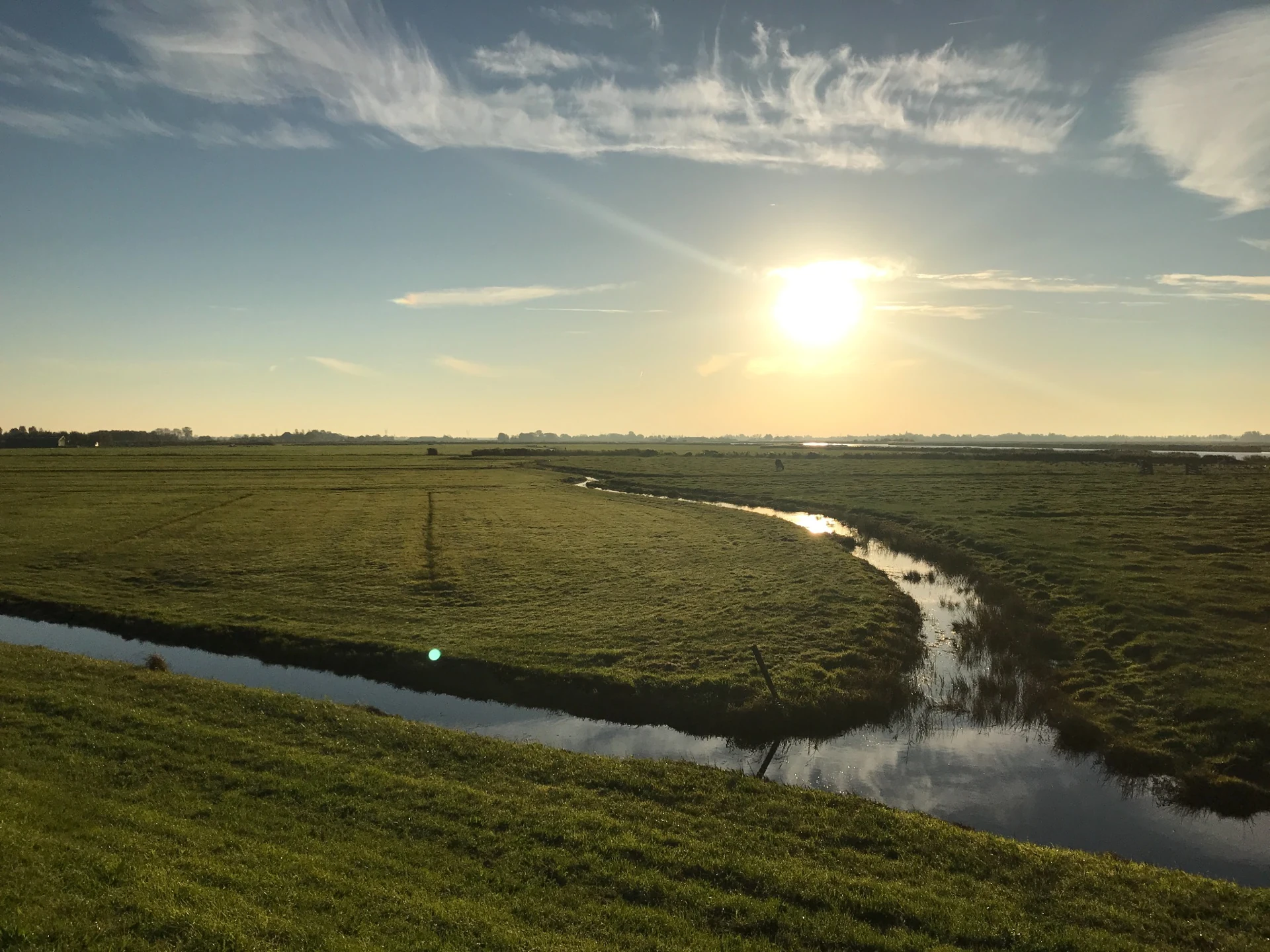 Sunlight over open polder fields and a winding waterway